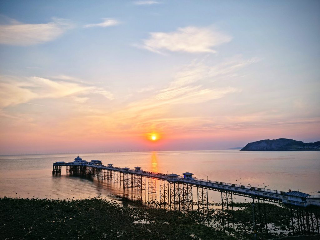 Sunrise over Llandudno Pier viewed from North Shore Promenade, with warm hues reflecting on the sea and Victorian architecture