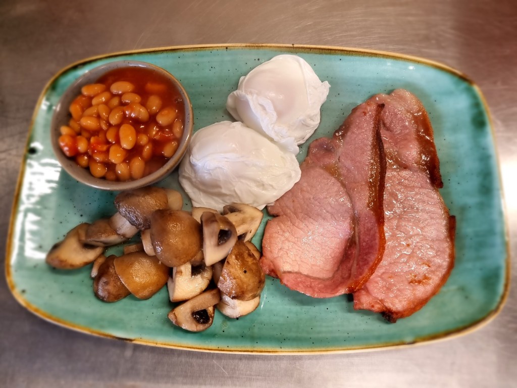 Smaller cooked breakfast served at Min y Don Llandudno B&B, featuring poached eggs, bacon, sautéed mushrooms, and baked beans