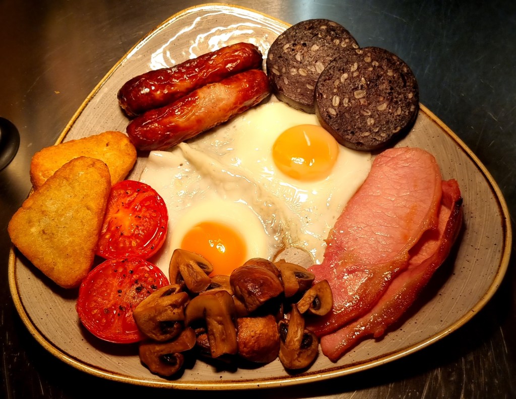 A full cooked breakfast served at Min y Don Llandudno B&B, featuring bacon, sausages, eggs, grilled tomato, mushrooms, hash browns, baked beans