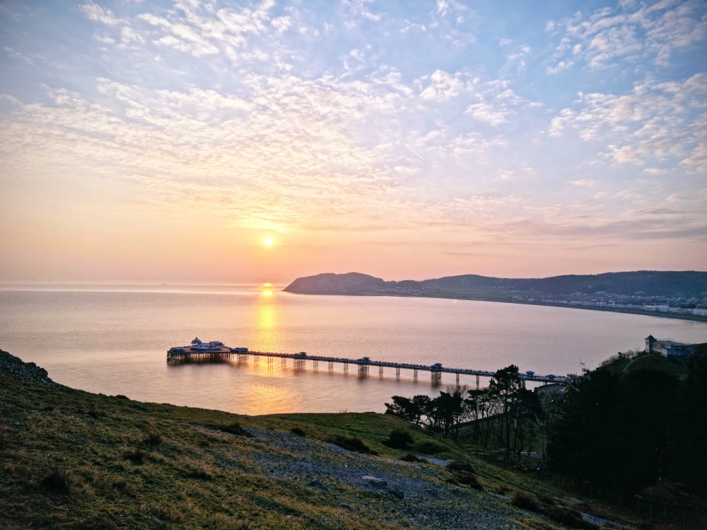 Sunrise view of Llandudno Pier, Little Orme, and townscape with Happy Valley gardens and the Lower Cable Car Station below, seen from the Great Orme