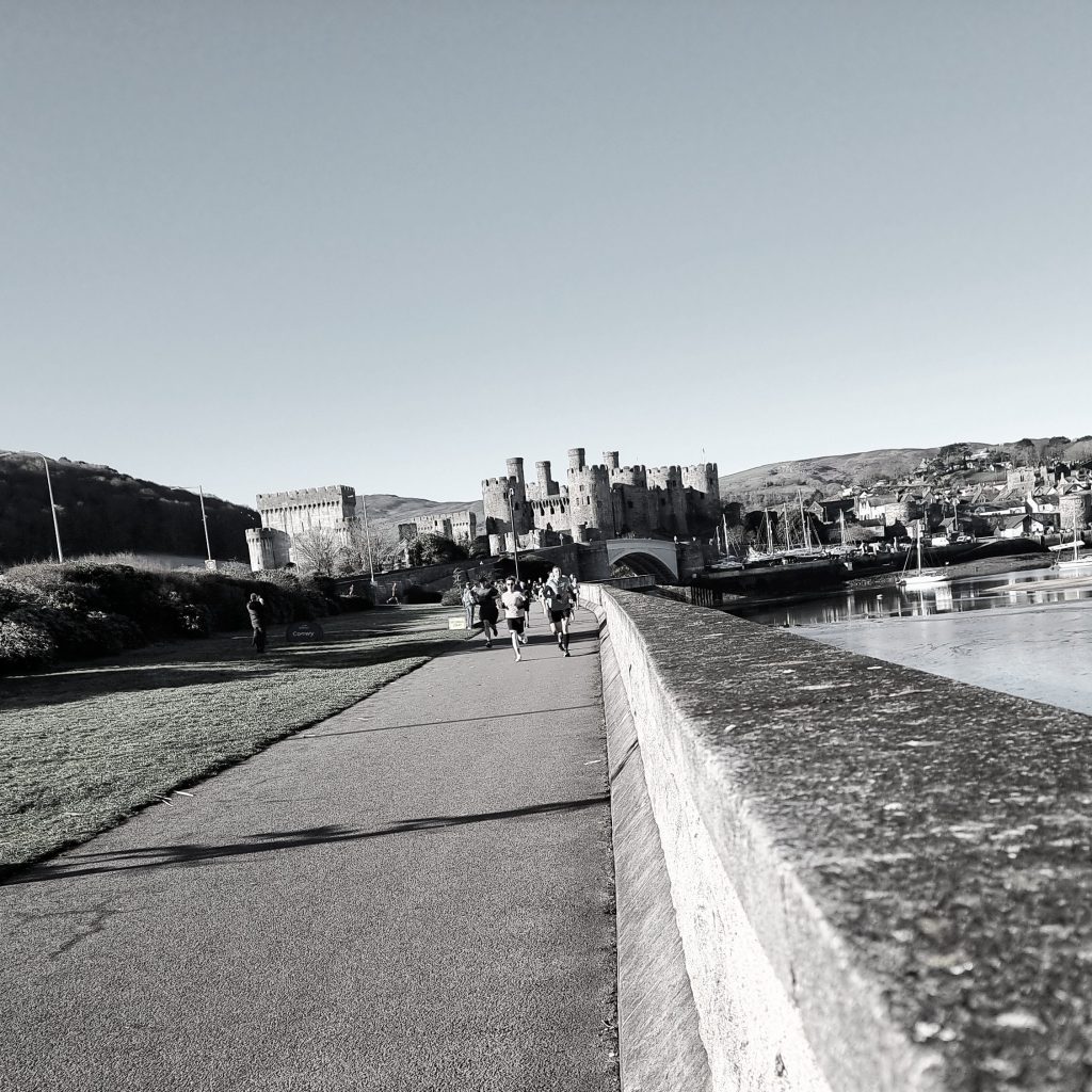 Runners taking part in Conwy Parkrun with Conwy Castle in the background near Llandudno