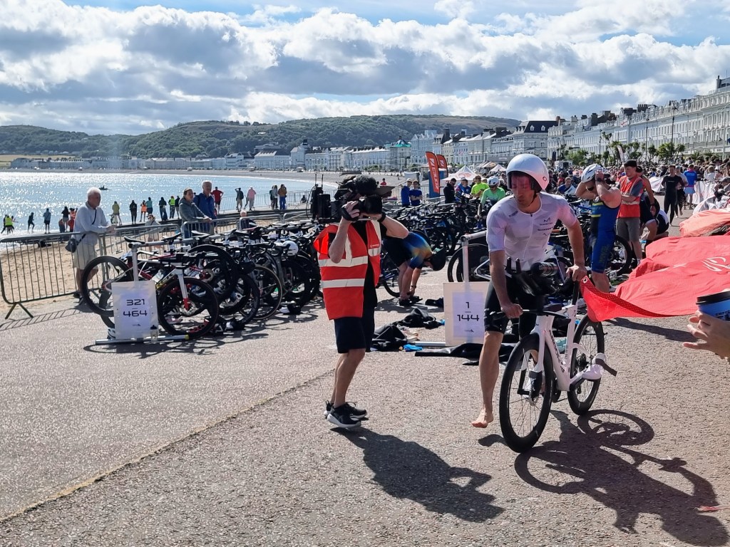 Triathletes in transition area after the swim, removing gear and preparing for the cycling stage in the Llandudno triathlon.