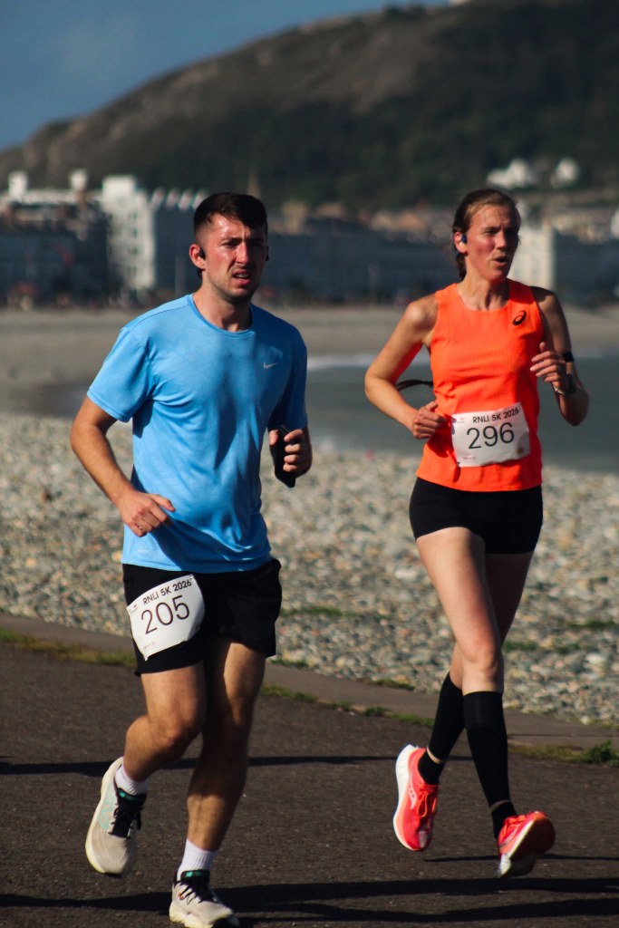 Teresa running along Llandudno Promenade during the RNLI Fun Run, smiling for the camera while competing in her first-ever timed 5K race.