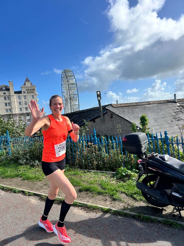 Teresa running along Llandudno Promenade near the turning point opposite Min y Don during the RNLI Fun Run, smiling for the camera despite racing conditions.